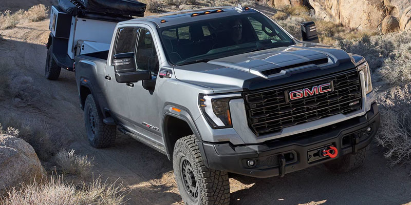 A grey 2026 GMC Sierra 3500 is hauling a small trailer up a dry dirt mountain terrain.