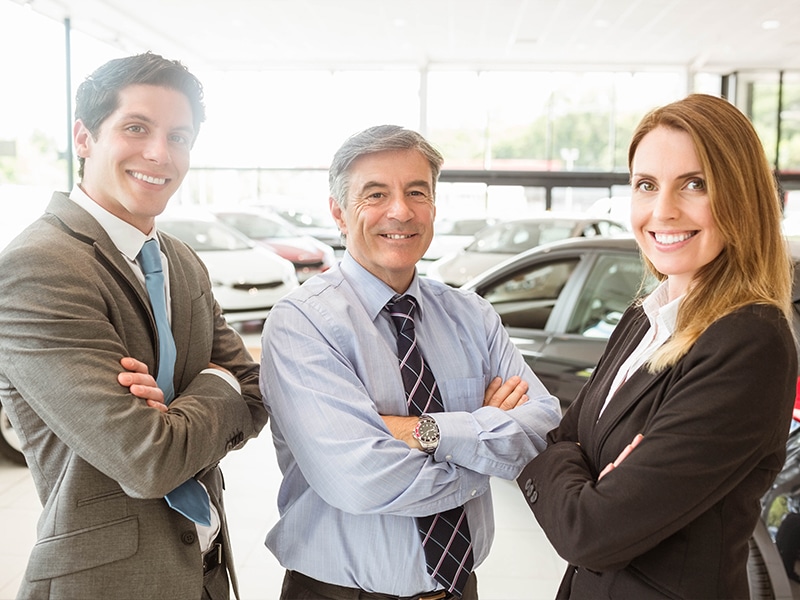 A GMC Professional Sales Rep team - 2 smiling men and a woman in the sunshine-filled showroom
